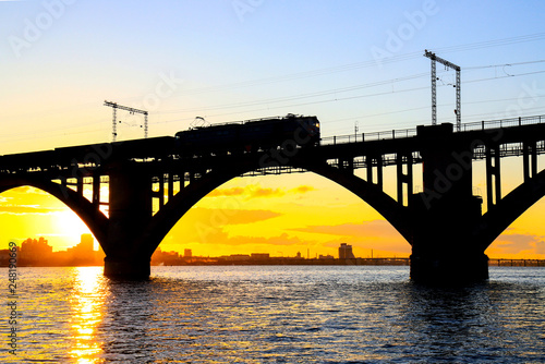 Fototapeta Naklejka Na Ścianę i Meble -  Silhouette of arched railway bridge and a train on the Dnieper river at beautiful sunset. Dnipo city, Dnepropetrovsk,  Ukraine.
