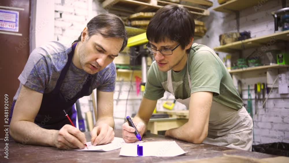 Two carpenters discuss drawing (round wood) in the workshop Two carpenters discuss drawing (round wood) in the workshop