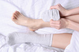 Female legs in white gray socks in white linens bed, top view