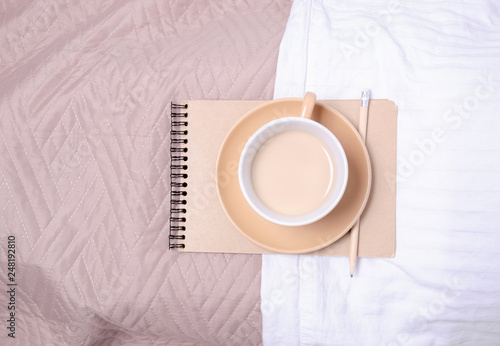 Cup of coffee witrh saucer notepad pencil on a white brown bed home design, top view photo