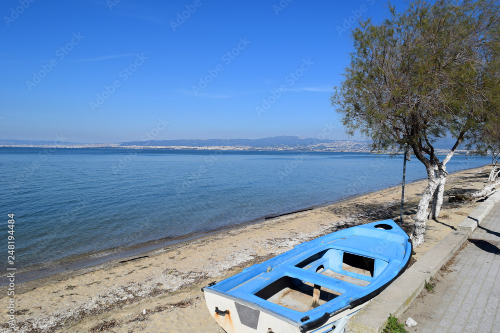 Abandoned fishing boat on beach in Peraia, Thessaloniki Greece. View of the city and the blue sea. 