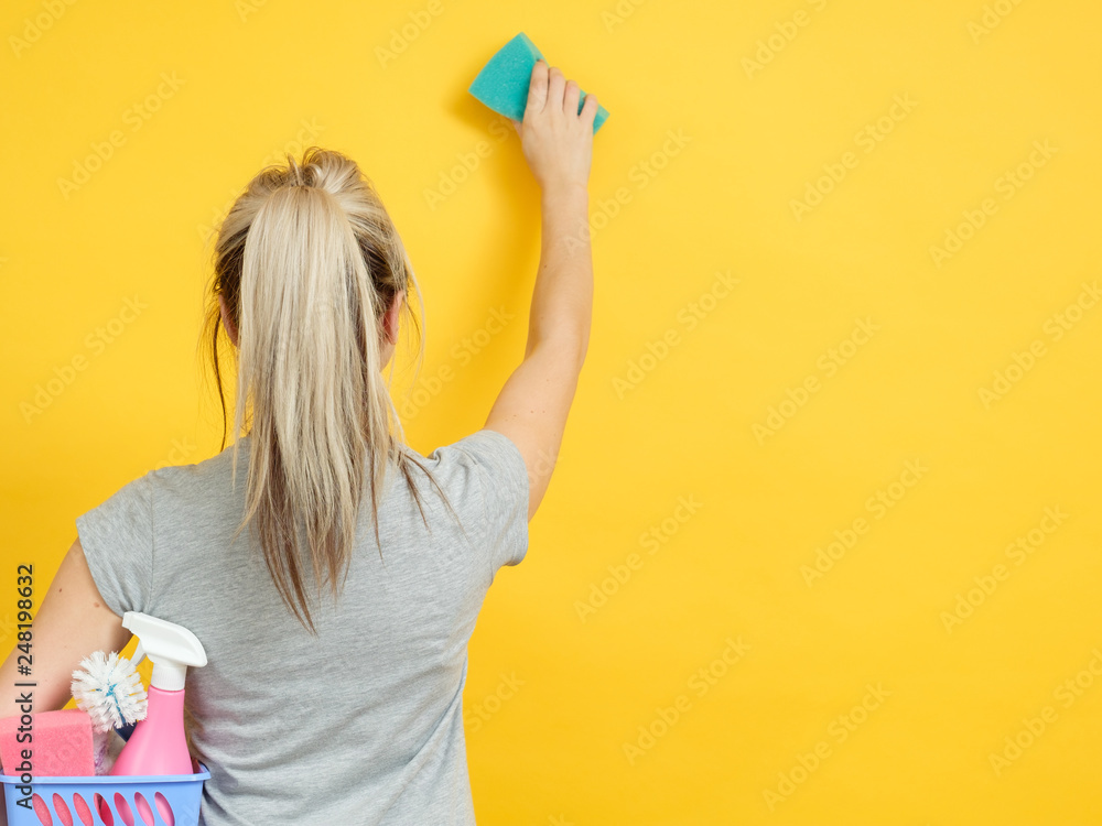 Home cleaning. Safe and efficient supplies. Woman with basket set raised hand wiping. Copy space on yellow background. Home cleaning. Safe and efficient supplies. Woman with basket set raised hand wiping. Copy space on yellow background.