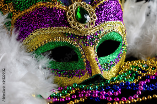Close up view of a jester mask with a white boa and color coordinating beads. Conceptual for Mardi Gras, carnival, or festival.