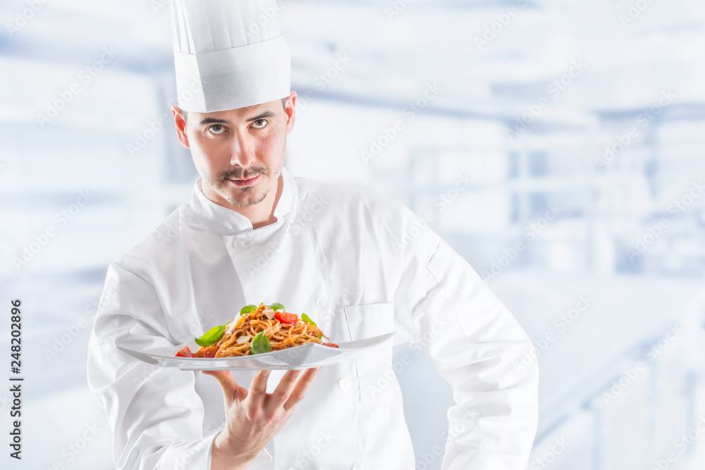Chef in restaurant kitchen holding plate with italian meal spaghetti bolognese