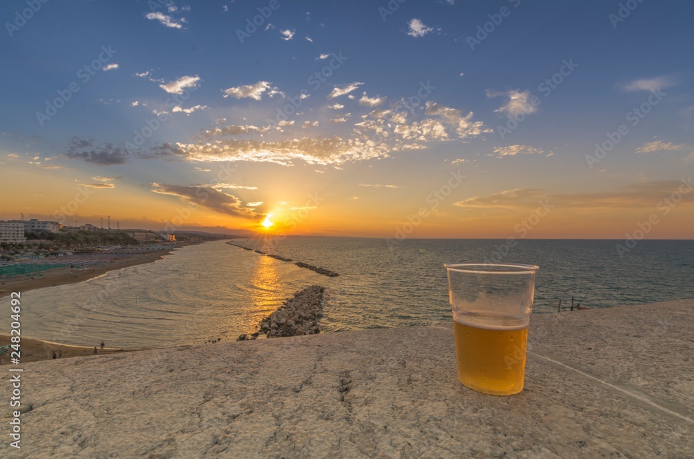 Bicchiere di birra sopra un muretto durante il tramonto Bicchiere di birra sopra un muretto durante il tramonto