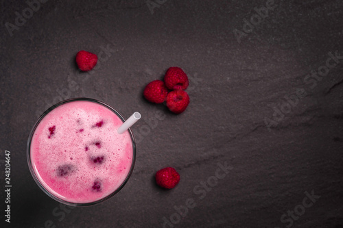 A glass of dairy free milkshake with fresh organic raspberries on a dark stone background with copy space