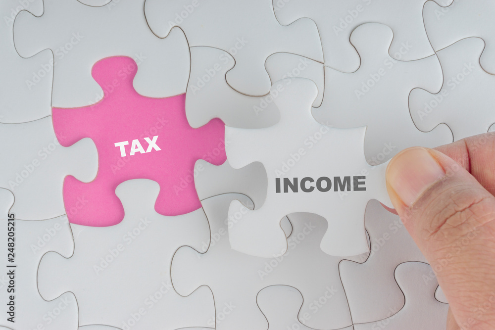 Hand holding piece of jigsaw puzzle with word INCOME TAX. Selective focus Hand holding piece of jigsaw puzzle with word INCOME TAX. Selective focus