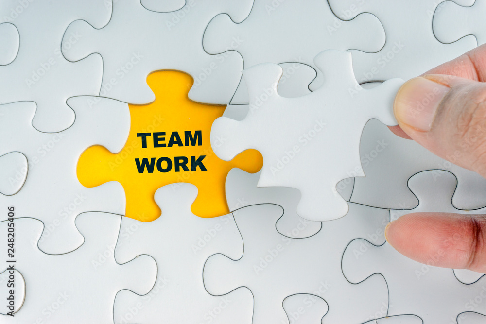 Hand holding piece of jigsaw puzzle with word TEAMWORK. Selective focus Hand holding piece of jigsaw puzzle with word TEAMWORK. Selective focus