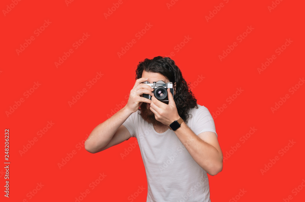 Young cheerful photographer with beard, while working in studio. Young brunette photographer is taking a photo Young cheerful photographer with beard, while working in studio. Young brunette photographer is taking a photo