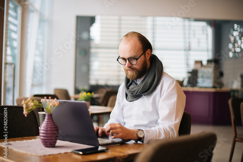 Wallpaper Mural Image of bearded man wearing glasses sitting in cafe while using laptop, freelancer in work. Torontodigital.ca