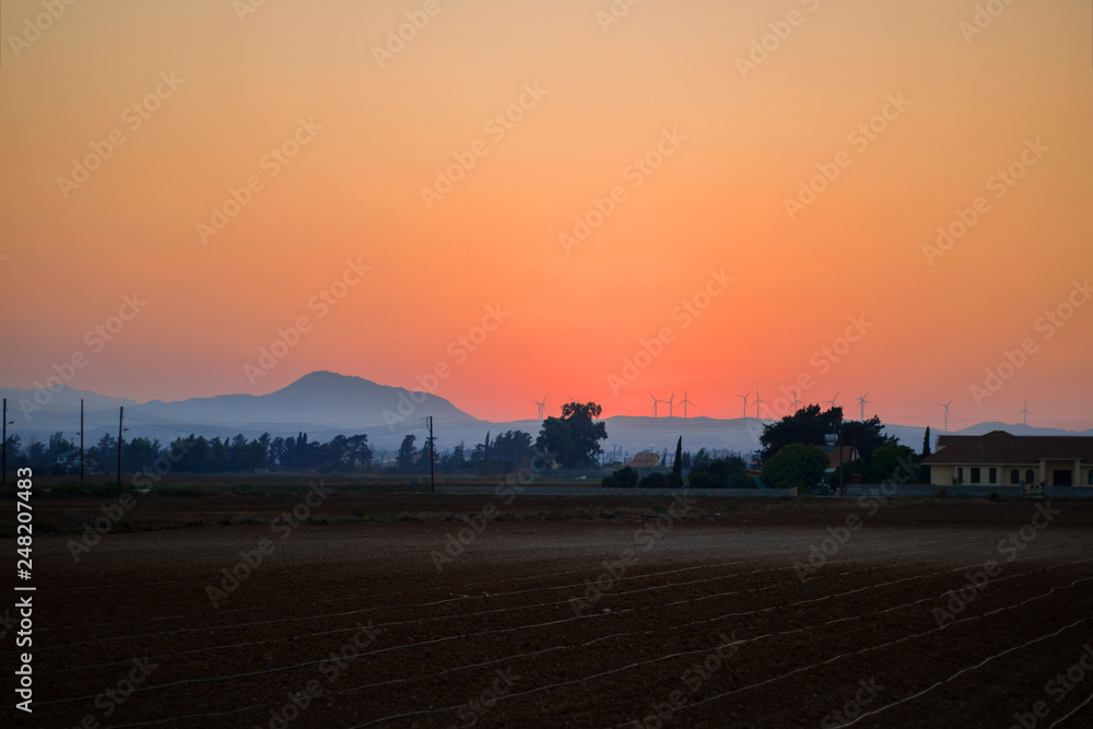Sunrise over the farm field, orange sky, fog, downy mildew, mountains, wind turbines. Horizontal. Mideterranian, cyprus, agriculture, ecology