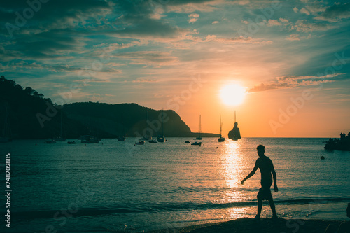 Quiet scene: Sailboats in a harbor at sunset with man silhouette.. Mediterranean sea of Ibiza island, cala benirras and Murada island. photo