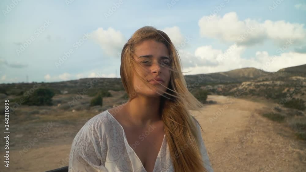 Portrait of young woman sitting at the bench, looking far. Beautiful landscape is on the background. Leisure of young lady. Camera moves to the left Portrait of young woman sitting at the bench, looking far. Beautiful landscape is on the background. Leisure of young lady. Camera moves to the left