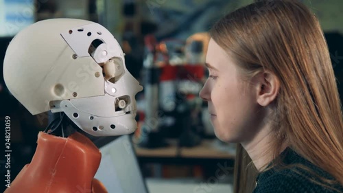 Female engineer looks at a droid working, side view.