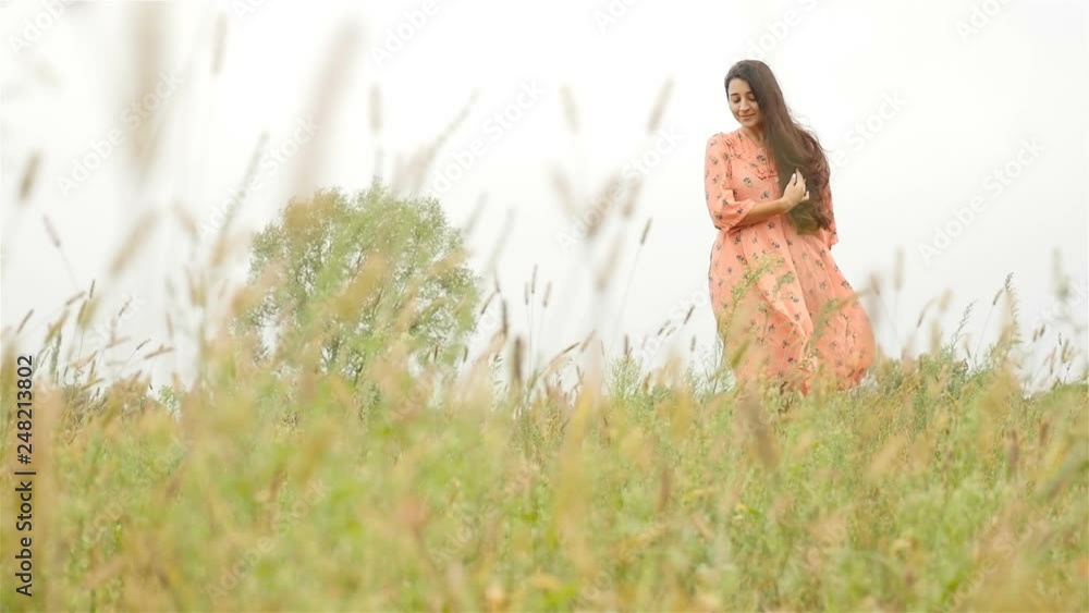 Beautiful girl walking on the green grass in the field. Slow motion. Tall brunette Beautiful girl walking on the green grass in the field. Slow motion. Tall brunette