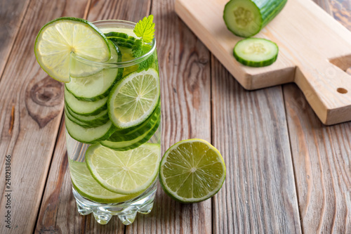 Glass of detox water with lime, cucumber and mint on wooden background illuminated by counter light. Soft focus.