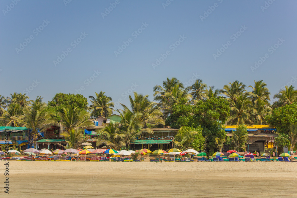 view of the colorful beach umbrellas with sun beds against the backdrop of restaurants and green jungle