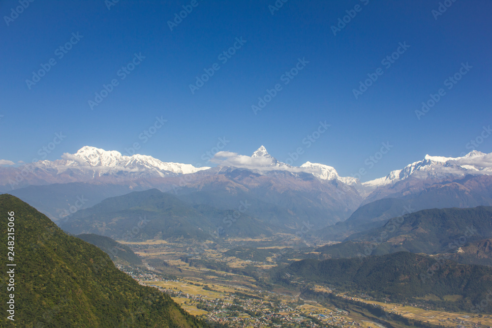 Fototapeta premium city in a green mountain valley on the background of the Annapurna snow ridge under a clear blue sky