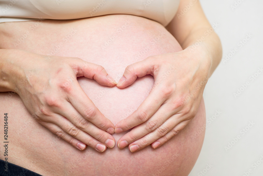 Woman holding her hands in a heart shape on her pregnant belly. Pregnant Belly with fingers Heart symbol. Maternity concept Woman holding her hands in a heart shape on her pregnant belly. Pregnant Belly with fingers Heart symbol. Maternity concept