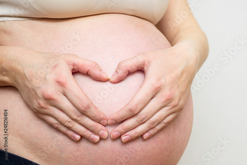 Wallpaper Mural Woman holding her hands in a heart shape on her pregnant belly. Pregnant Belly with fingers Heart symbol. Maternity concept Torontodigital.ca