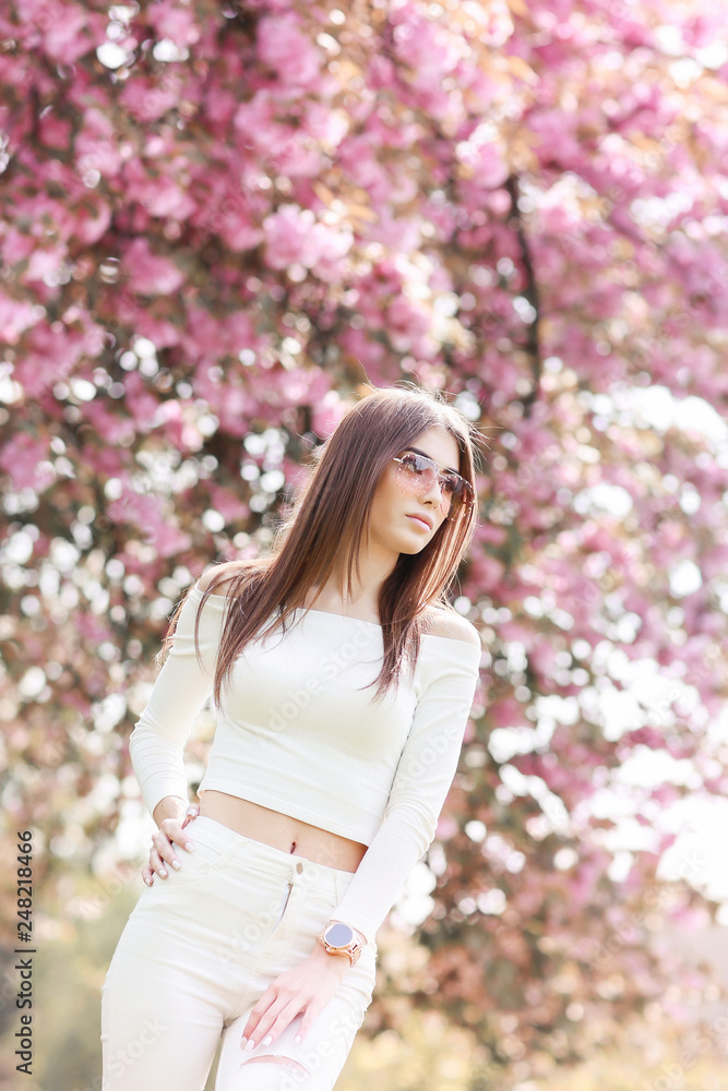 Outdoor portrait of young beautiful happy smiling lady posing near flowering tree. Model wearing stylish accessories clothes. Girl closed her eyes. Female beauty fashion concept. City lifestyle. Outdoor portrait of young beautiful happy smiling lady posing near flowering tree. Model wearing stylish accessories clothes. Girl closed her eyes. Female beauty fashion concept. City lifestyle.