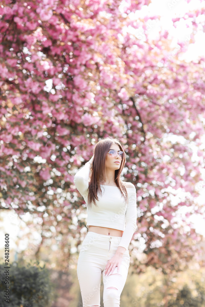 Outdoor portrait of young beautiful happy smiling lady posing near flowering tree. Model wearing stylish accessories clothes. Girl closed her eyes. Female beauty fashion concept. City lifestyle. Outdoor portrait of young beautiful happy smiling lady posing near flowering tree. Model wearing stylish accessories clothes. Girl closed her eyes. Female beauty fashion concept. City lifestyle.