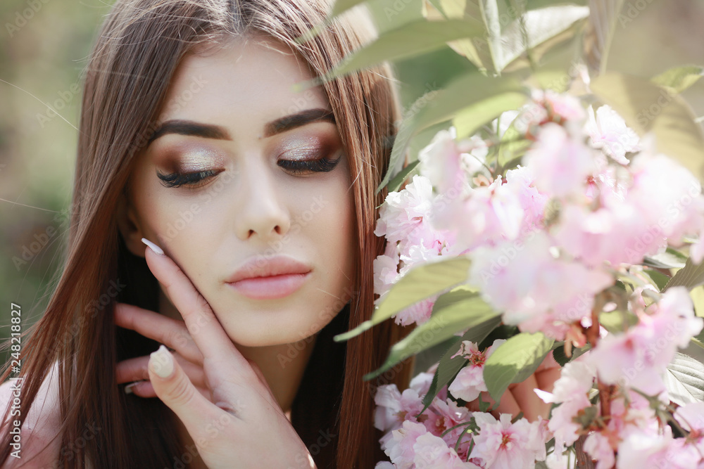 The beautiful girl with a romantic hairstyle and a professional make-up enjoys a smell of pink colors in a garden. The girl dreams. A portrait of the beautiful girl model in the spring in the park. The beautiful girl with a romantic hairstyle and a professional make-up enjoys a smell of pink colors in a garden. The girl dreams. A portrait of the beautiful girl model in the spring in the park.