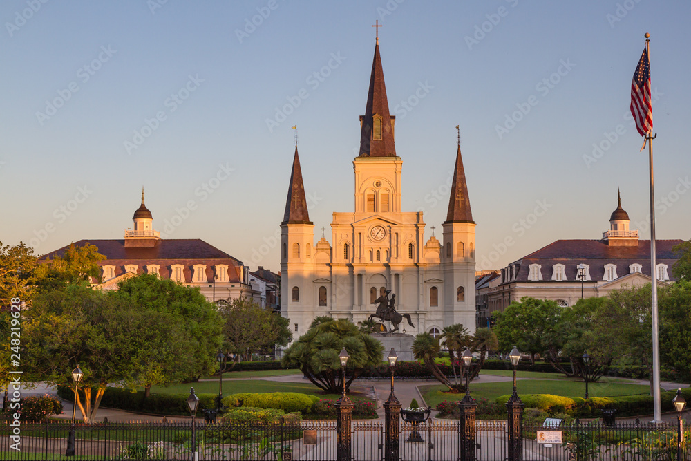St. Louis Cathedral in Jackson Square within the French Quarter of New Orleans, Louisiana, USA. Golden morning light bathes the cathedral, American flag on right side of church, no people. Horizontal.