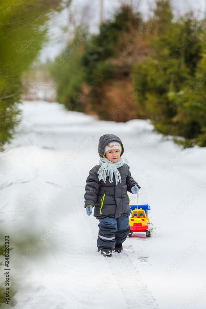 Smiling boy walks on snowy street with toy dump trucks