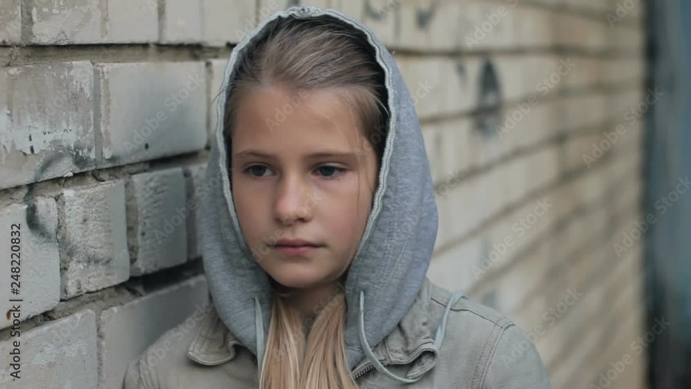 Sad depressed young girl thinking about problems leaning head against brick wall. Close up portrait of upset child wearing hooded sweatshirt outdoors. Sad depressed young girl thinking about problems leaning head against brick wall. Close up portrait of upset child wearing hooded sweatshirt outdoors.