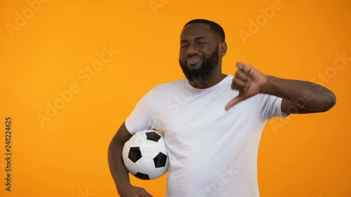 African-American man playing with soccer ball and showing thumbs down, losing