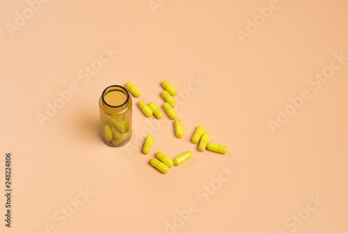 Yellow pills in the glass bottle on a orange background.