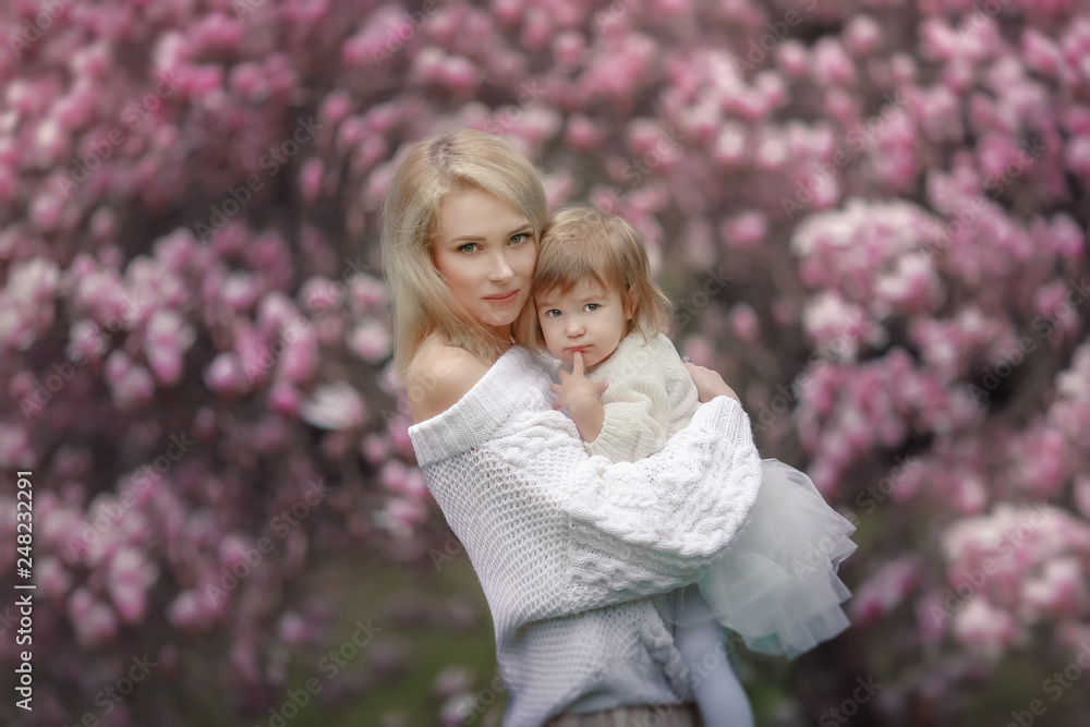Portrait of happy joyful child in white clothes over tree flowers blossom background. Family playing together outside. Mom cheerfully hold little daughter Newborn spring concept Portrait of happy joyful child in white clothes over tree flowers blossom background. Family playing together outside. Mom cheerfully hold little daughter Newborn spring concept