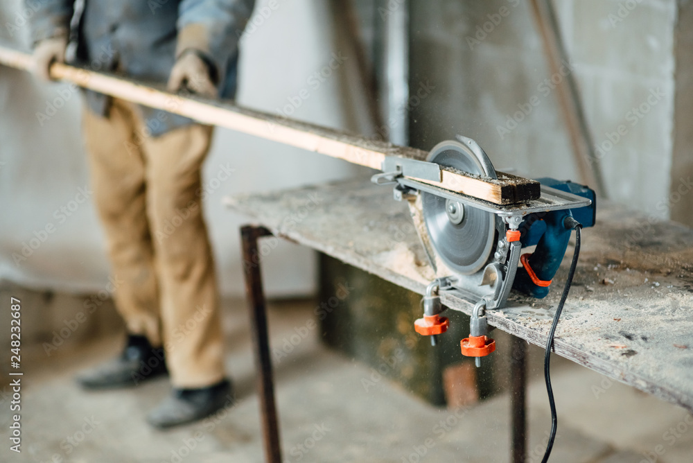 man in work clothes by profession carpenter handles wooden board on circular saw on a wooden workshop table, joiner works on machine in factory man in work clothes by profession carpenter handles wooden board on circular saw on a wooden workshop table, joiner works on machine in factory