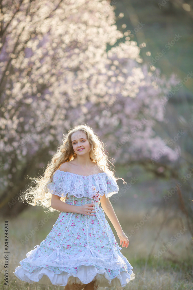 Sweet woman in a beautiful dress, walking through the park with flowers in hands