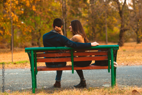 Couple holding hand and sitting on bench in autumn park.