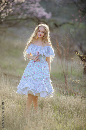 A young long-haired blonde is walking in a blooming garden. Dress and hair fluttering like in a fairy tale © ElenaBatkova