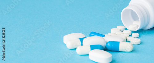 Close up pills spilling out of pill bottle on blue background. Medicine, medical insurance or pharmacy concept photo