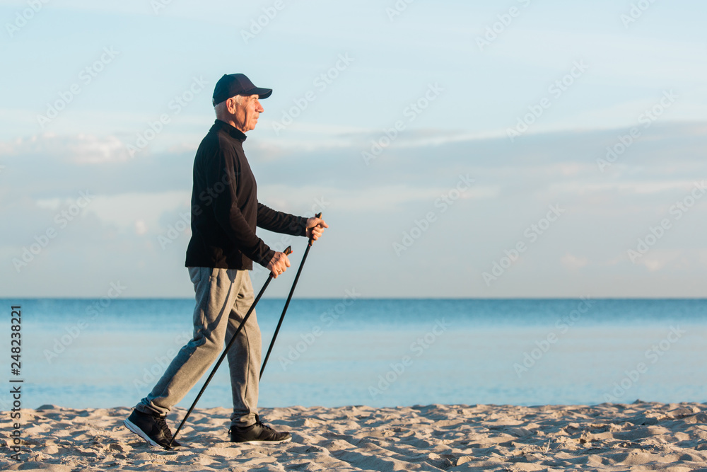 Nordic walking - senior man working out on beach. Healthy lifestyle