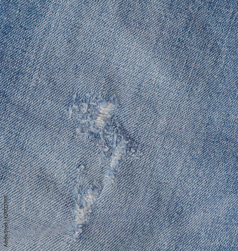 Hole and Threads on Denim Jeans. Ripped Destroyed Torn Blue jeans background. Close up blue jean texture
