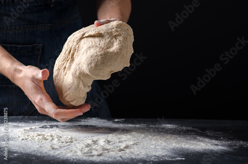 Woman kneading dough on sprinkled with flour table. Yeast dough for bread, rolls, pizza, focaccia or pie. Homemade dough. Design for text.