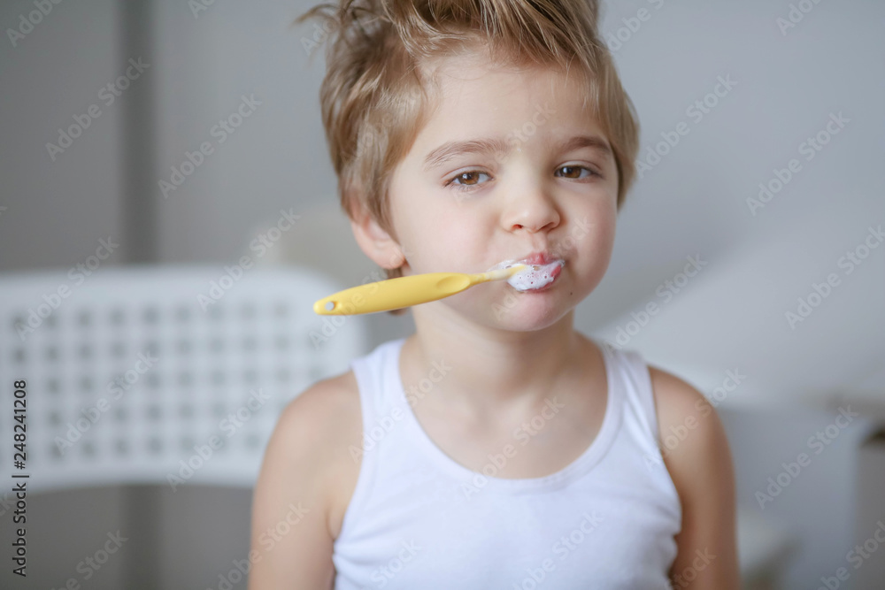 Close up portrait of cute, adorable, toddler boy wearing denim overalls, long T-shirt, sitting on the floor, brushing his teeth with a toothbrush Close up portrait of cute, adorable, toddler boy wearing denim overalls, long T-shirt, sitting on the floor, brushing his teeth with a toothbrush