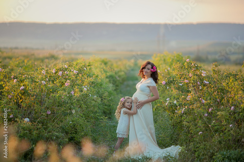 Happy pregnant woman with little daughter in a green tea rose garden