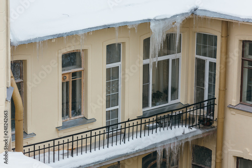 Photo of big icicles hanging from building, many people get injured by the drop of icicles/ poor attic insulation, danger for humans, long icicles hang from the roof of a house, winter concept.