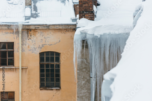Huge human sized icicles hang from a residential building, during the thaw the ice can break off and cripple a person/ danger for humans, long icicles hang from the roof of a house, winter concept © Denis Mamin
