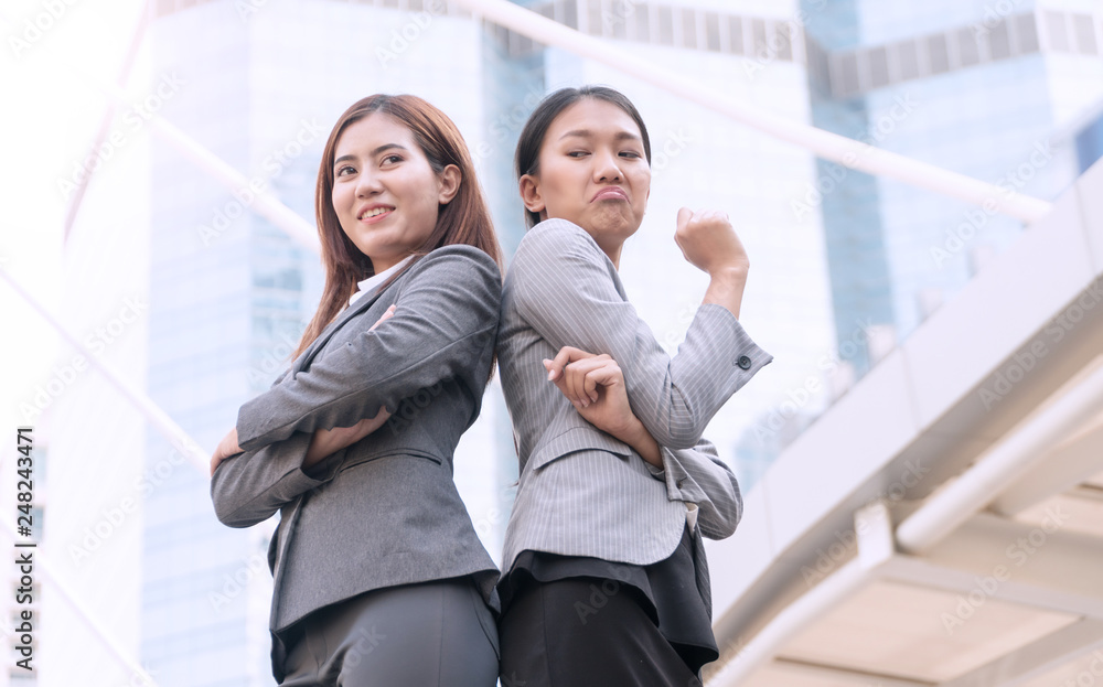 Serious two young business woman standing back to back with crossed arms ignoring each other on modern city background Serious two young business woman standing back to back with crossed arms ignoring each other on modern city background