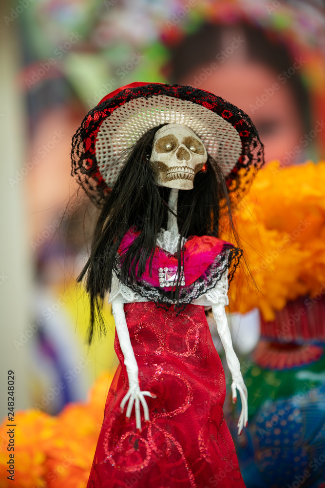 Mexican skeleton figure in national headdress and red dress isolated on the background of a bouquet of orange flowers.