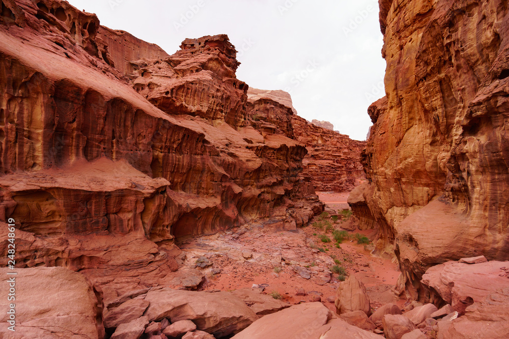 Canyon in Wadi Rum desert, Jordan, Middle East, The Valley of the Moon. Orange sand, haze, clouds. Designation UNESCO World Heritage Site. Red planet Mars landscape. Canyon in Wadi Rum desert, Jordan, Middle East, The Valley of the Moon. Orange sand, haze, clouds. Designation UNESCO World Heritage Site. Red planet Mars landscape.