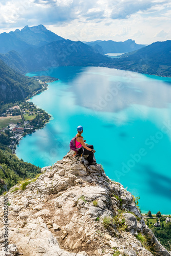 Via ferrata female climber enjoying the views over lake Attersee, Austria, with blue waters, in a bright, hot, Summer day. Perfect Summer destination for rock and water activities.