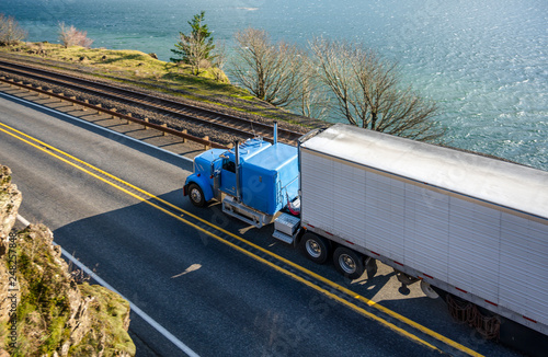 Blue classic big rig with reefer semi trailer transporting cargo running on the road along the Columbia River
